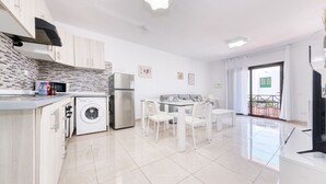 A modern kitchen with a washing machine, a refrigerator, and a dining area with a glass table and chairs. - Happy Beach Home - Shared pool By LVH (Puerto del Carmen)