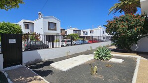 A residential street with white houses, a black gate, and a cactus in the foreground. - Happy Beach Home - Shared pool By LVH (Puerto del Carmen)