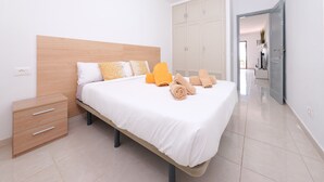 A neatly made bed with white and yellow bedding, a wooden headboard, and a bedside table with drawers. - Happy Beach Home - Shared pool By LVH (Puerto del Carmen)