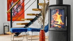 Una sala de estar moderna con un sofá azul, un jarrón rojo con plantas secas, una chimenea negra y una escalera con escalones de madera.