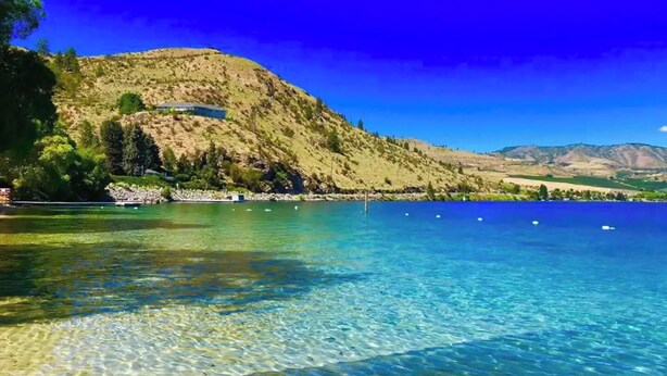 Ein klarer See mit einem Berg im Hintergrund und einem kleinen Gebäude am Ufer.