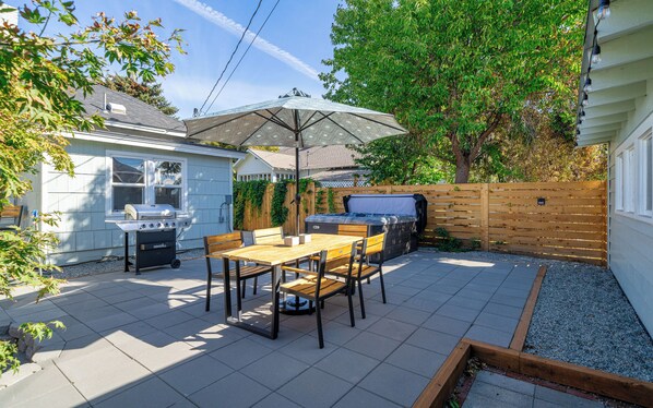 A backyard with a barbecue grill, a hot tub, and a patio table with chairs.