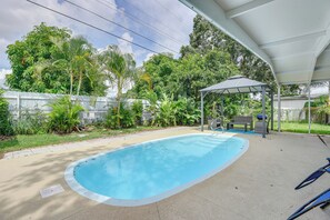 En swimmingpool med ett täckt uteområde, omgiven av frodig grönska och en inhägnad trädgård.