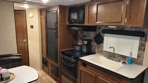 A compact kitchen with a refrigerator, microwave, stove, and sink. - A well-maintained, cozy camper  in a secluded location near state land (Grayling)