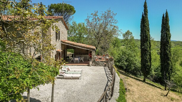 A stone house with a terrace, outdoor seating, and a view of the countryside.