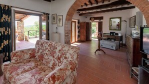A spacious living room with a floral sofa, a wooden coffee table, and a TV. An arched brick fireplace and a stone pillar are visible.