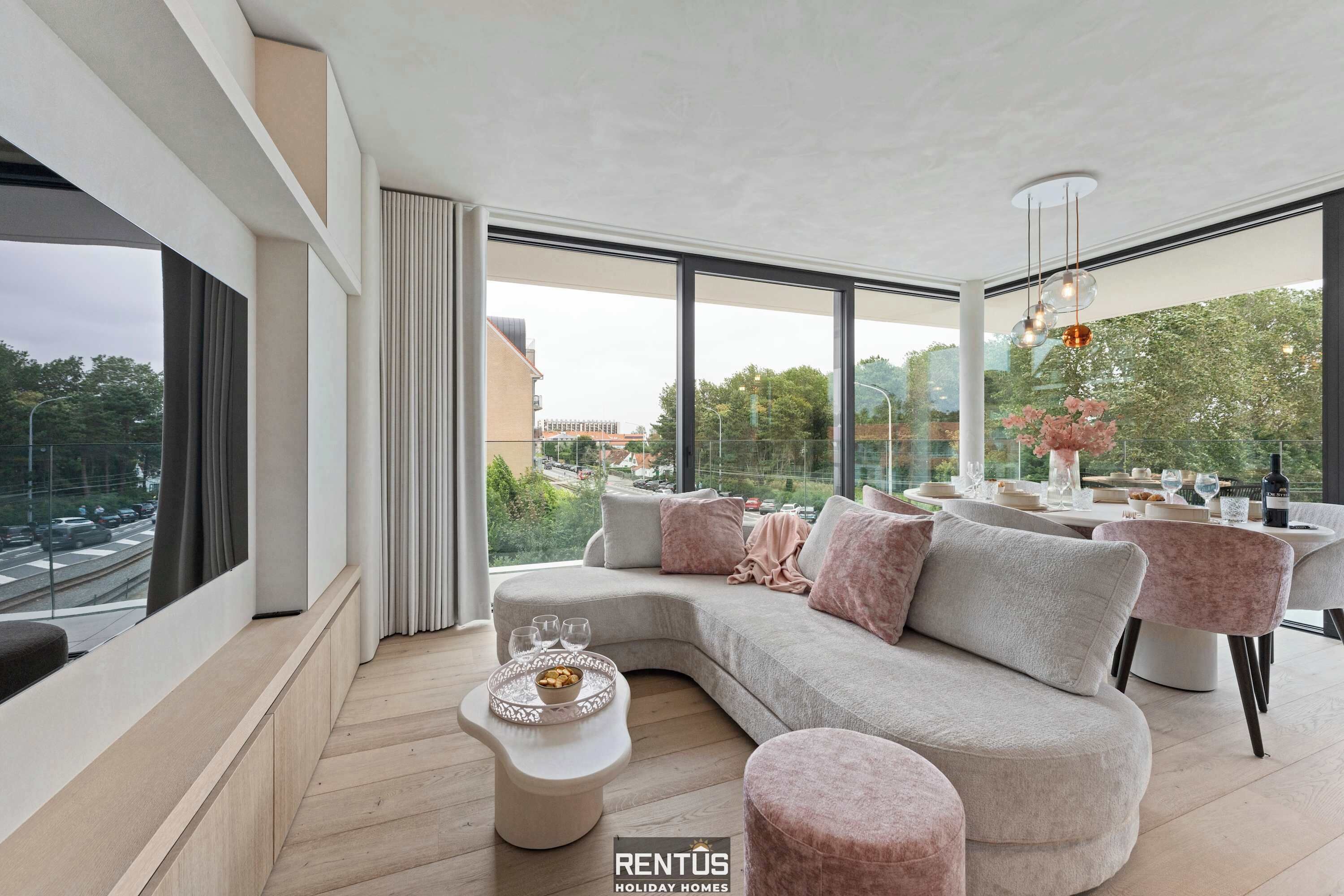 Una sala de estar moderna con un amplio sofá modular, una mesa de comedor con sillas y vistas a la ciudad a través de grandes ventanales.