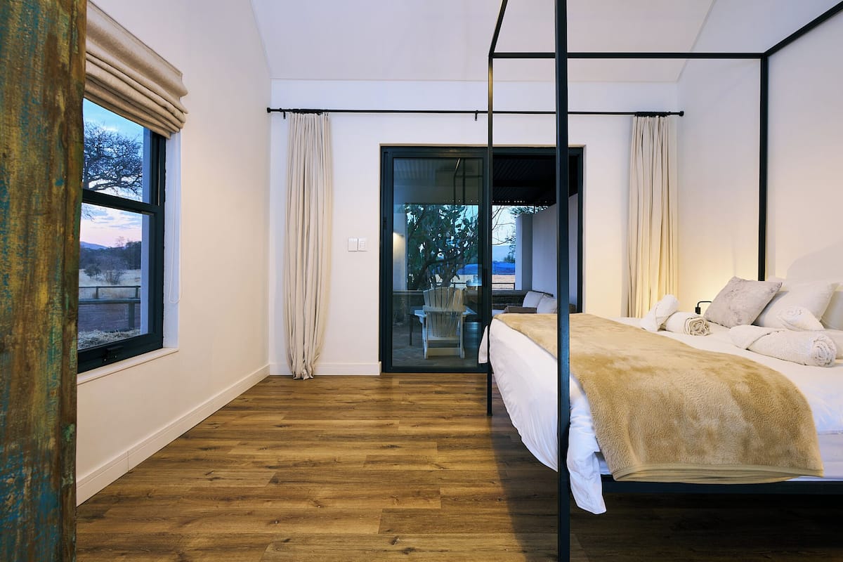 A modern bedroom with a wooden floor, a bed with white linens, and a view through a glass door to an outdoor area.