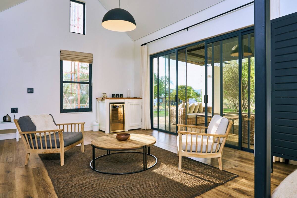A modern living room with a fireplace, wooden furniture, and large glass doors leading to an outdoor area.