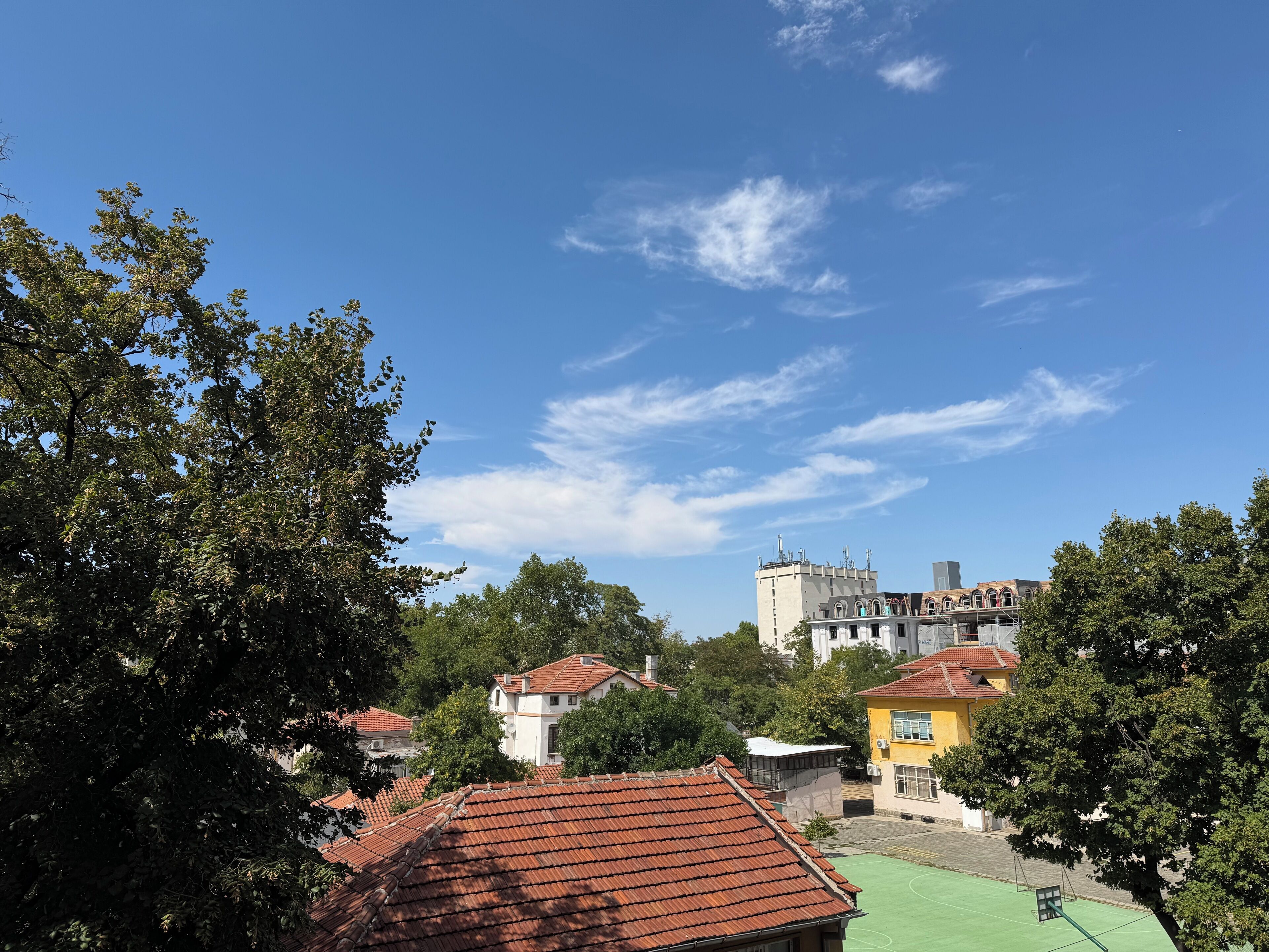 Ein Innenhof mit roten Ziegeldächern, umgeben von Bäumen und Gebäuden unterschiedlicher Architektur.