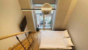 A bedroom with a bed, a desk, a chair, and a window overlooking a parking area.