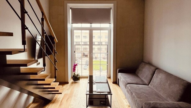 A modern living room with a wooden staircase, a grey sofa, and a glass coffee table.