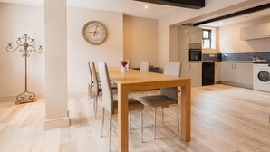 A modern kitchen with a dining area, wooden flooring, and a clock on the wall.