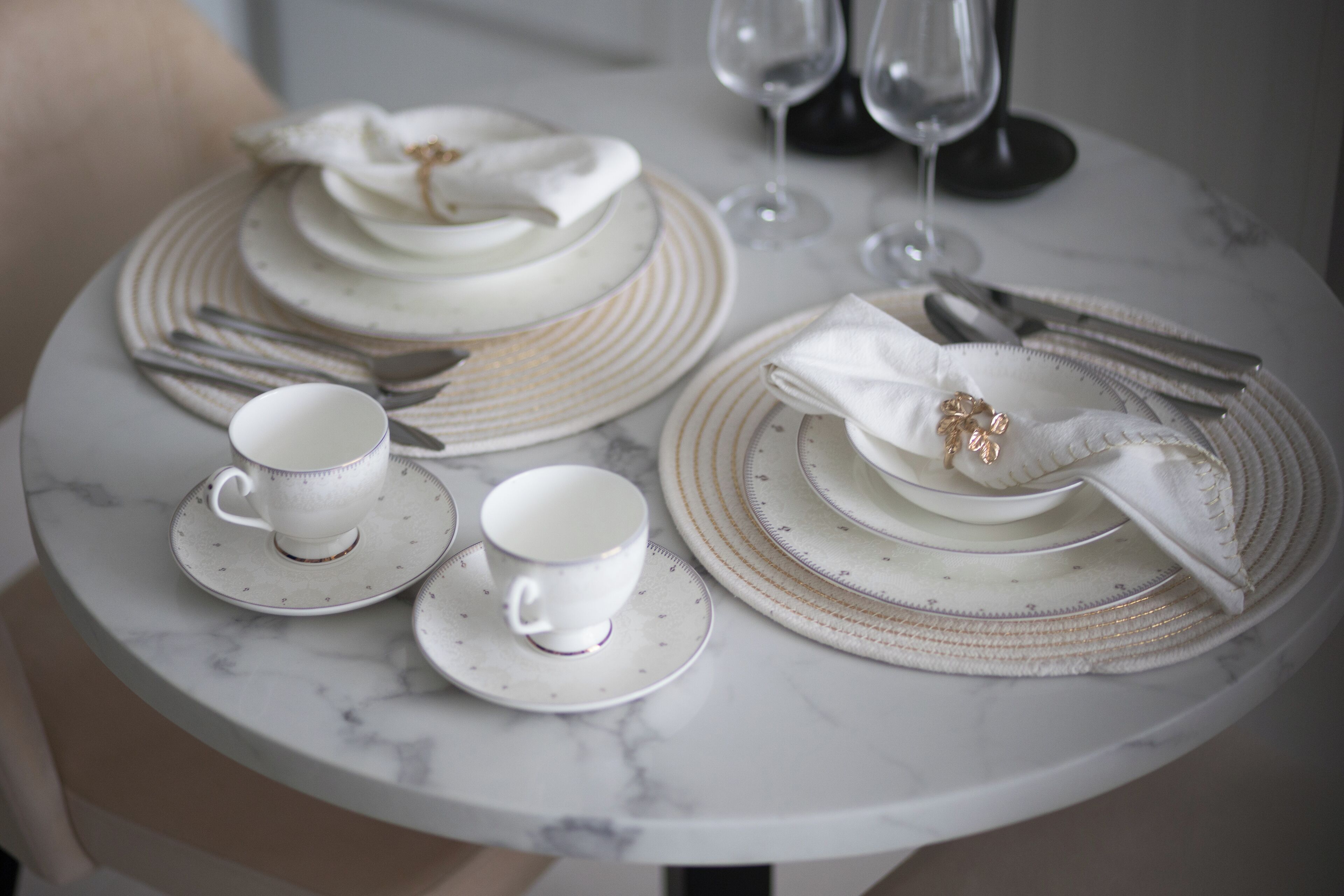 A round marble table set with white plates, cups, and a folded napkin.