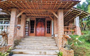 A traditional wooden staircase leading to a brick entrance with a wooden door. - Omah Trasan Pangrango (Ciawi)