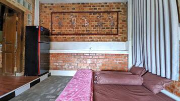 Een kamer met een bakstenen muur, een bed met roze en bruine beddengoed, een zwarte koelkast, en een raam met gordijnen.