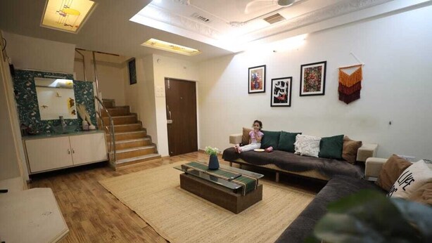 A living room with a sofa, a coffee table, a staircase, and a door. - Daisy Duplex (Nagpur)