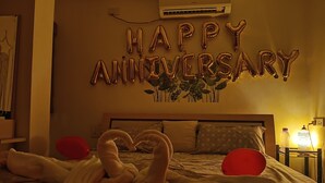 A bedroom with a bed, pillows, a wall decoration, and a nightstand with a lamp. - Daisy Duplex (Nagpur)