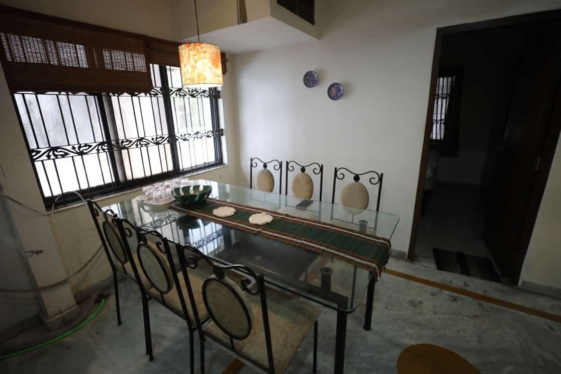A dining area with a glass table and metal chairs, a hanging light fixture, and a window with decorative bars.