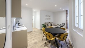 Una cocina moderna con estufa integrada, un comedor con mesa redonda y sillas amarillas, y una sala de estar con sofá y planta.