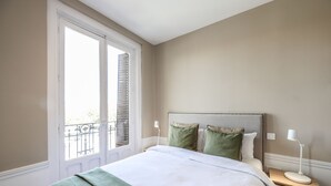 Un dormitorio con cama, mesitas de noche, una ventana con contraventanas y vistas al exterior.