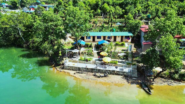A riverside hotel with a dock, outdoor seating, and a view of the surrounding greenery. - Lake Wave Cottage & Resturent (Lekhnath)