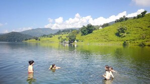 A lake with people swimming, surrounded by green hills and a clear sky. - Lake Wave Cottage & Resturent (Lekhnath)