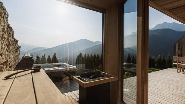 Una terraza de madera con un jacuzzi y una mesa, con vistas a un paisaje montañoso.