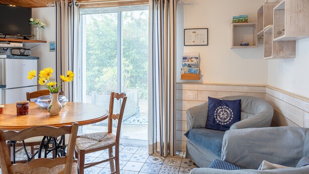 A cozy living room with a wooden ceiling, a dining table with chairs, a sofa, and a television. - Holiday Home 'Gîte Tout Confort 800m Plage' with Private Terrace and Private Garden (L'Épine)
