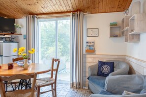 A cozy living room with a wooden ceiling, a dining table with chairs, a sofa, and a television.