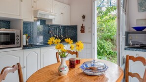 A kitchen with white cabinets, a microwave, a stove, and a dining table with a vase of flowers. - Holiday Home 'Gîte Tout Confort 800m Plage' with Private Terrace and Private Garden (L'Épine)