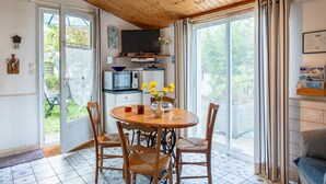 A dining area with a wooden table and chairs, a television above the table, and a view through the glass doors. - Holiday Home 'Gîte Tout Confort 800m Plage' with Private Terrace and Private Garden (L'Épine)