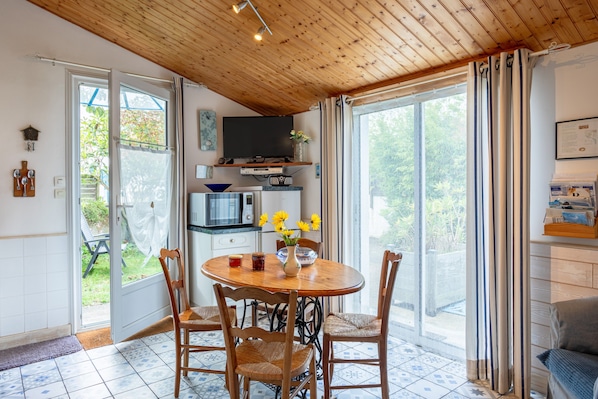 A dining area with a wooden table and chairs, a television above the table, and a view through the glass doors.
