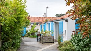 A narrow alleyway with a wooden bench, a planter box, and a building with blue shutters. - Holiday Home 'Gîte Tout Confort 800m Plage' with Private Terrace and Private Garden (L'Épine)