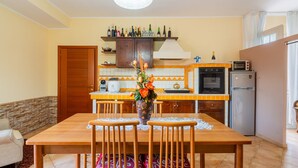 A kitchen with a dining table, chairs, a vase with flowers, a refrigerator, a microwave, and a stove. - Apartment 'Casula Salento' with Private Garden, Wi-Fi and Air Conditioning (matino)