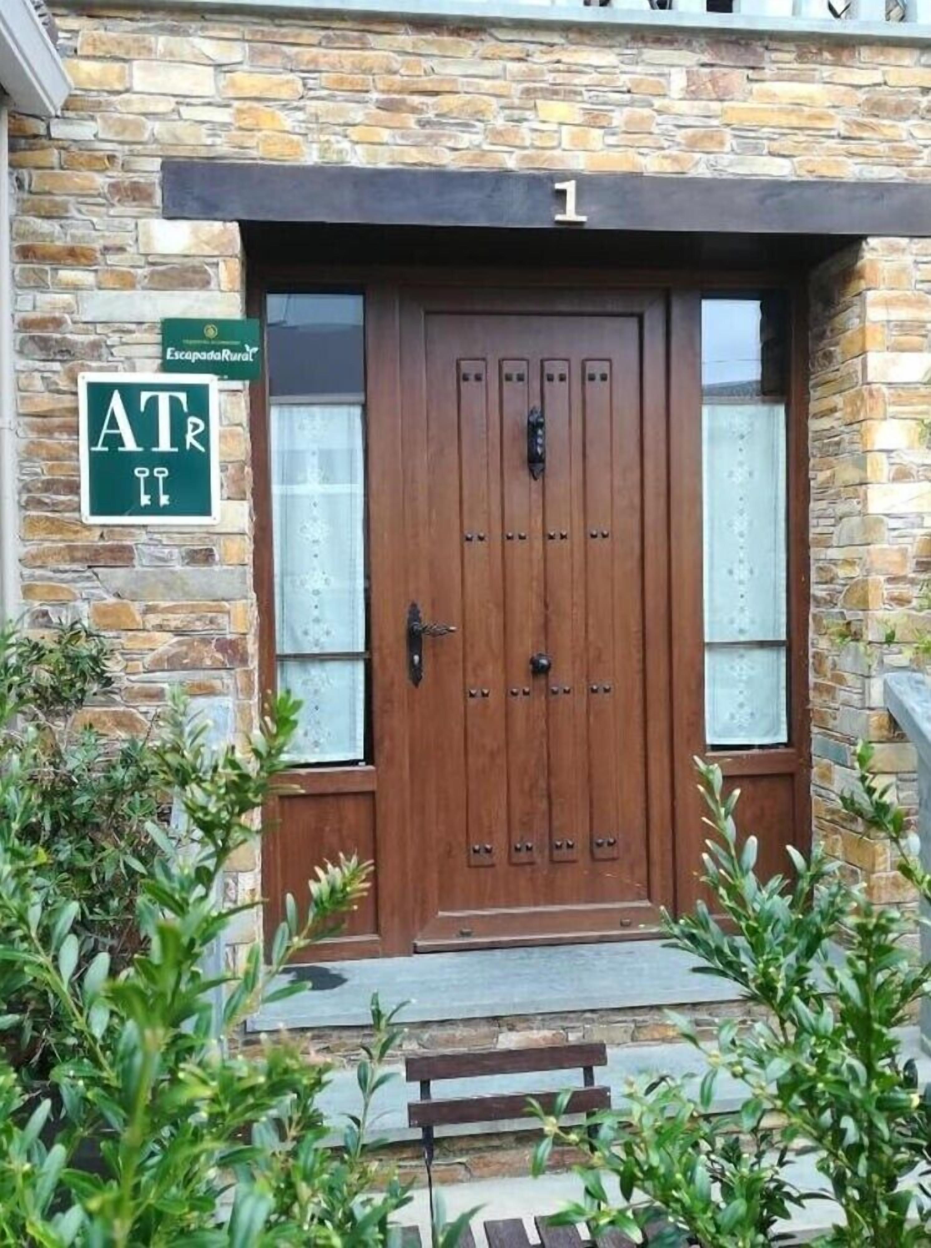 A stone building with a wooden double door, a bench in front, and a sign indicating a location.