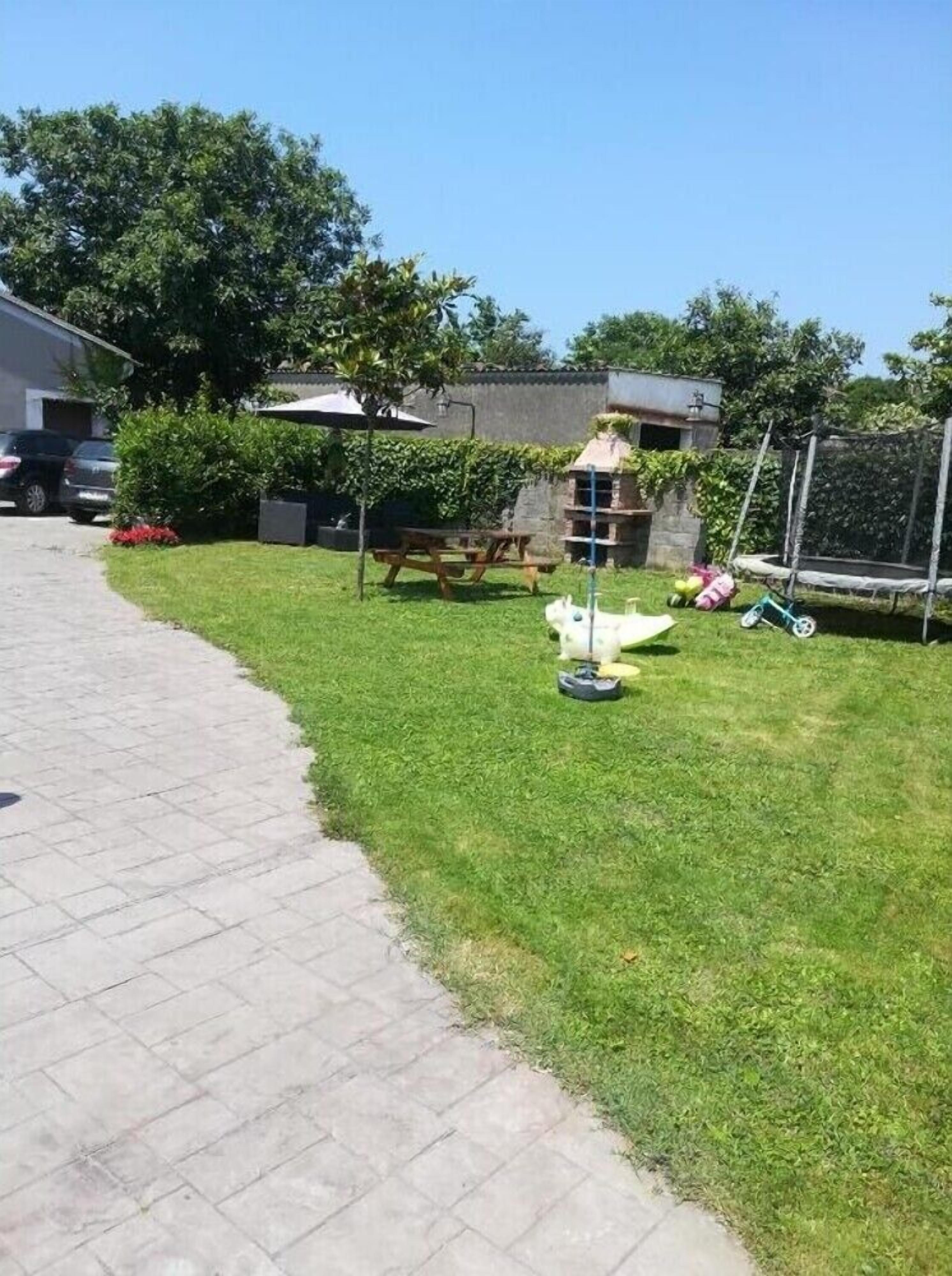 Un vialetto lastricato conduce a un'area verde con un piccolo parco giochi, un tavolo da picnic e un'area recintata per bambini.