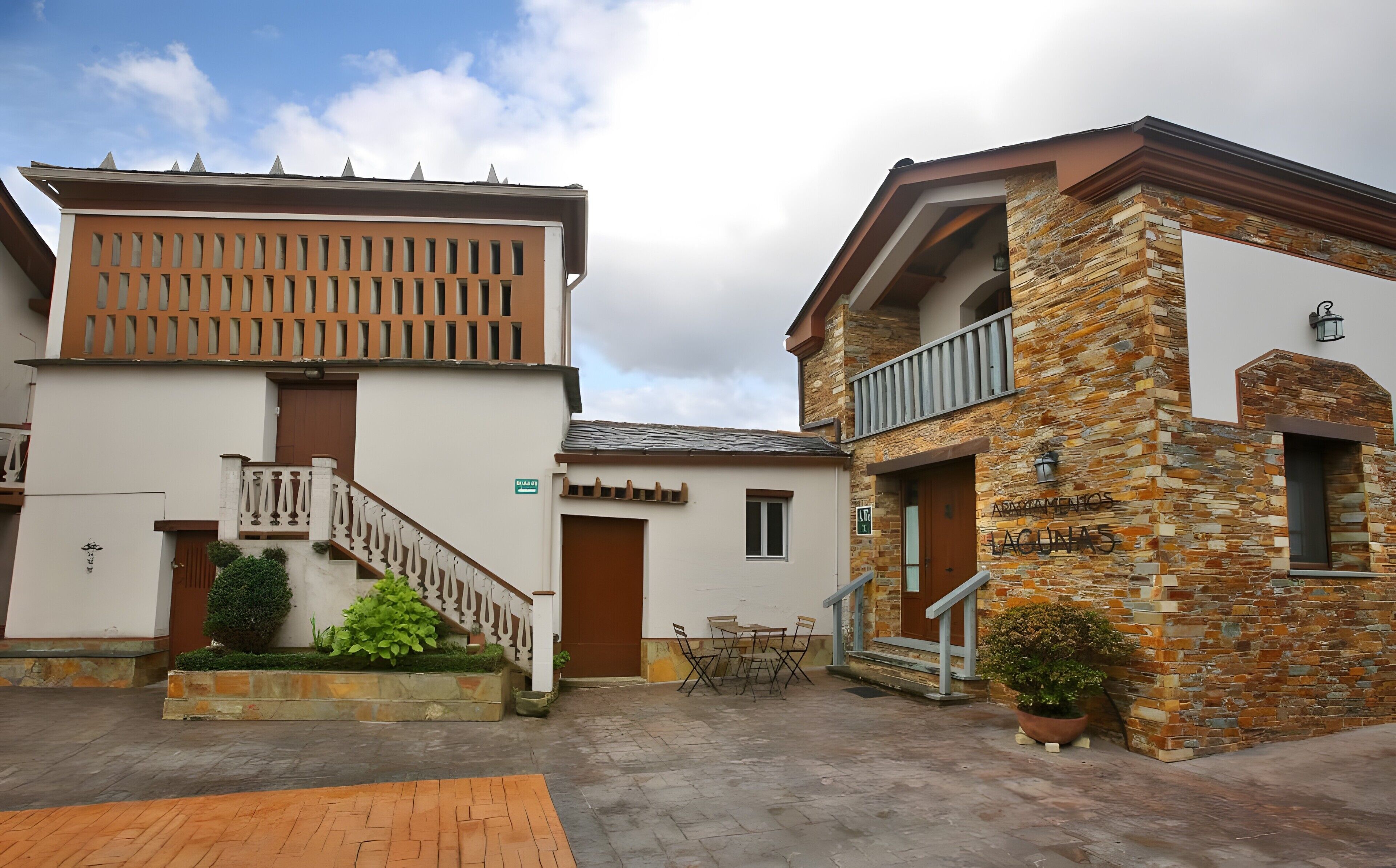 Un patio con una escalera que lleva a un edificio de fachada de piedra y un balcón.