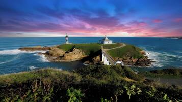 Un paysage côtier avec un phare et un bâtiment blanc sur une île verdoyante, entourée d’eau.