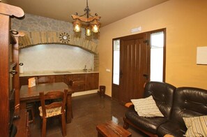 Un coin repas avec une table et des chaises en bois, un canapé en cuir noir, une cheminée en pierre et une porte en bois.