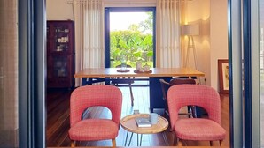 Un comedor con una mesa, dos sillas rojas, una araña y vistas a zonas verdes exteriores.