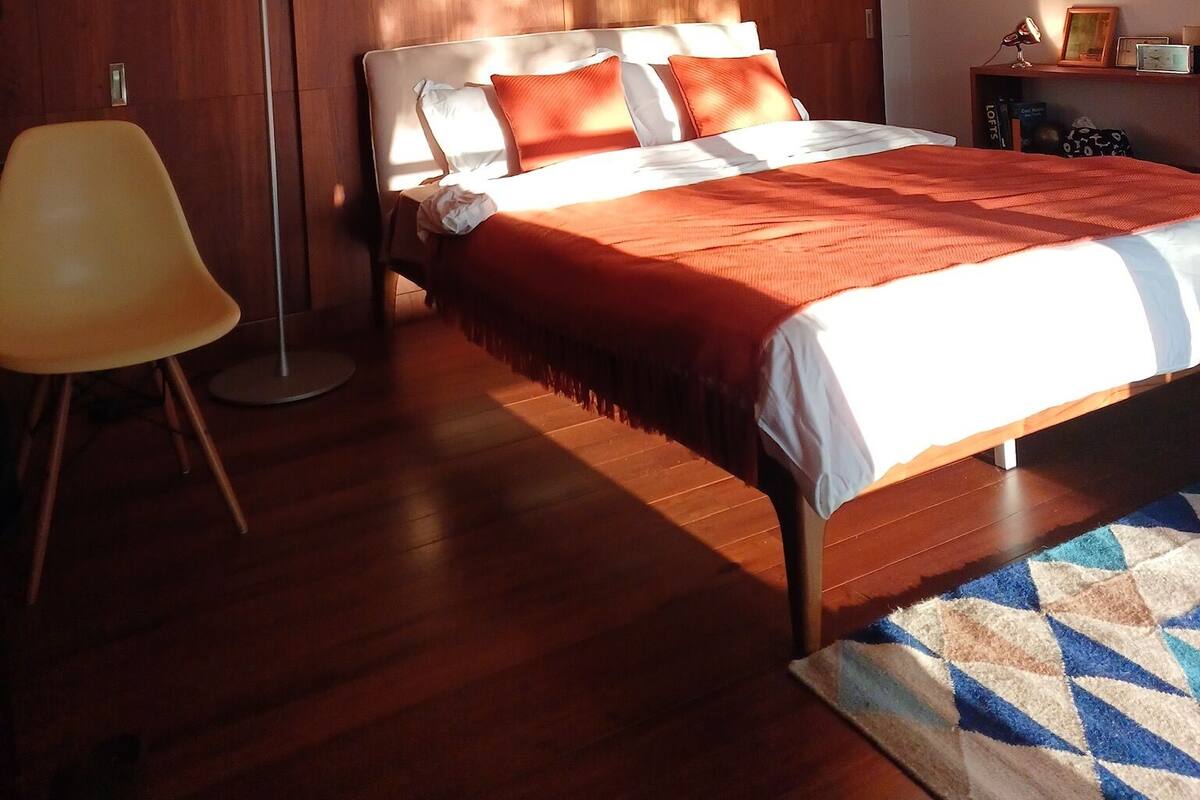 A bedroom with a bed, a floor lamp, a chair, and a rug.