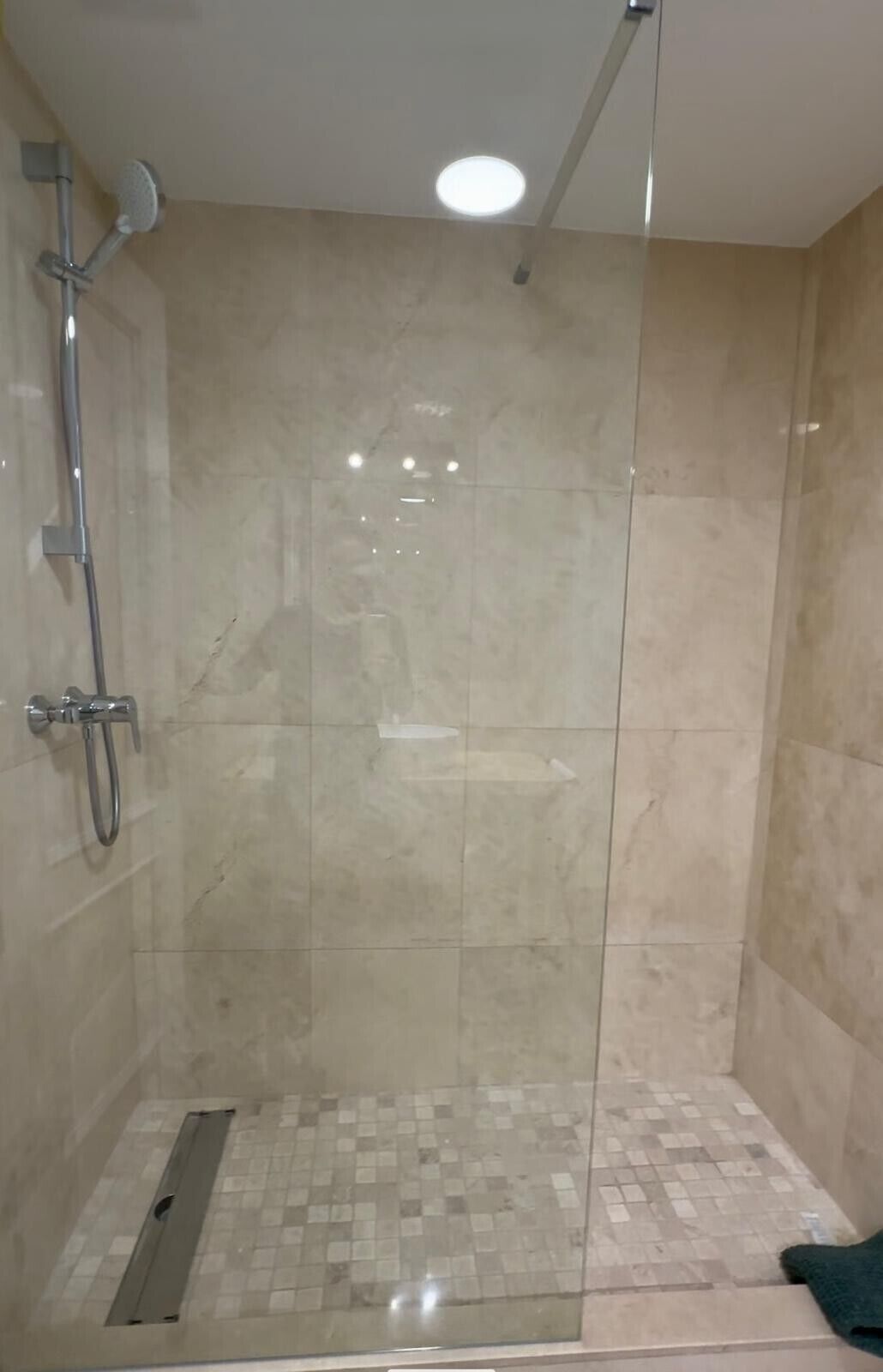Une douche fermée par des parois en verre, avec un sol carrelé, une douchette à main et un robinet fixé au mur.