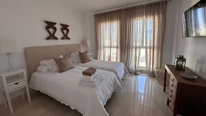 A bedroom with two beds, a nightstand, a dresser, and a TV on the wall.