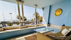 A balcony with a glass table, a sofa, and a view of a marina with boats.
