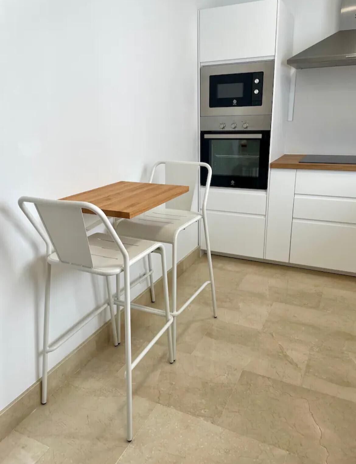 Une petite cuisine équipée d’un four à micro-ondes, d’un four et de meubles blancs. On y trouve une table en bois avec deux chaises.