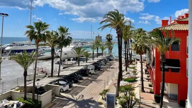 A marina with parked boats, palm trees, and a red building.