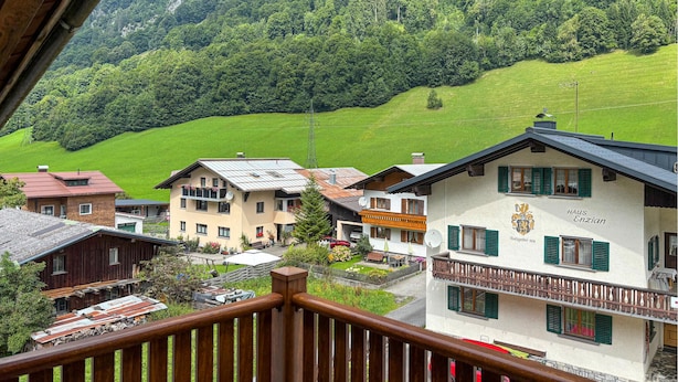A traditional European building with a balcony, surrounded by lush green hills and a clear sky.