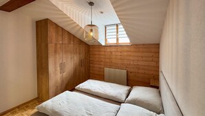 A bedroom with a loft bed, wooden wardrobe, and a slanted ceiling with a skylight.