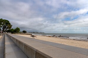 Une plage avec une promenade en béton, une vue sur l’océan et une côte rocheuse visible au loin.